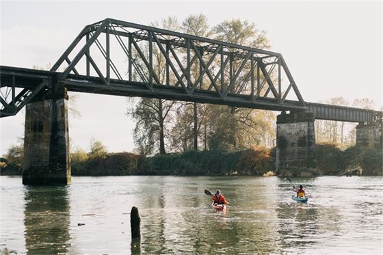 Two kayakers paddling in the Snohomish River beneath the old trestle bridge